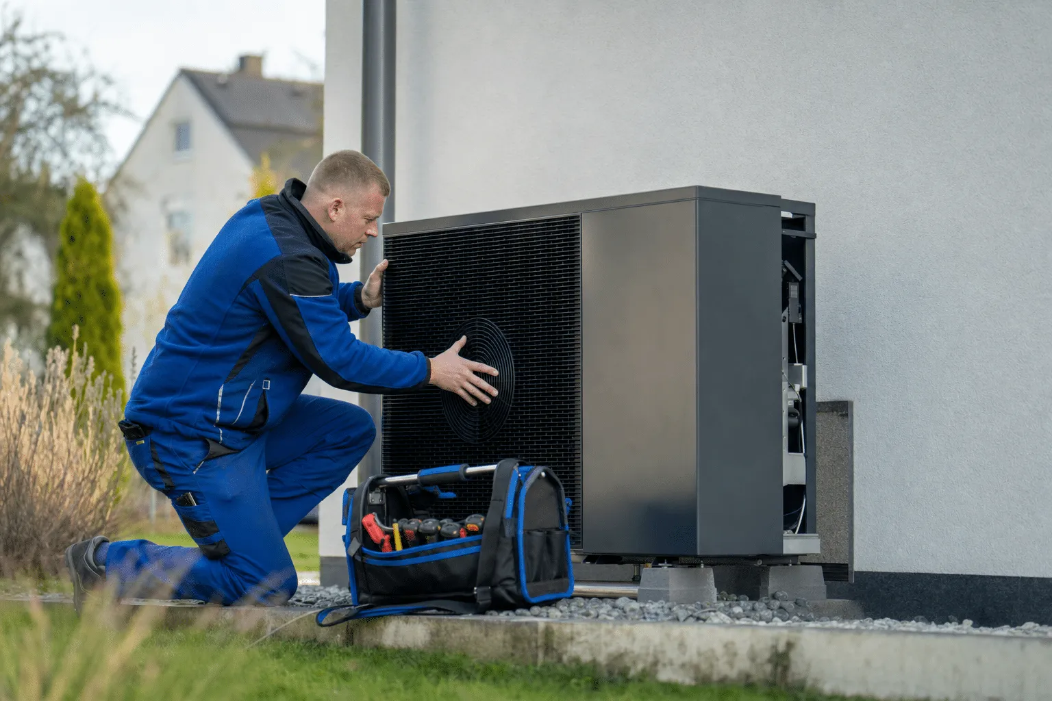 Installateur montiert eine moderne Wärmepumpe neben einem Einfamilienhaus