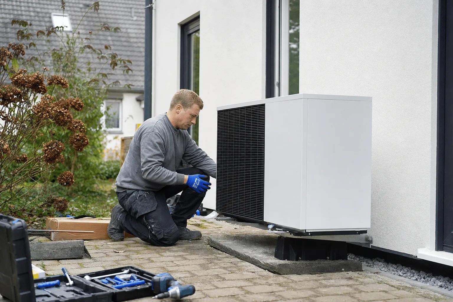 Installateur montiert Außeneinheit einer Wärmepumpe neben einem Einfamilienhaus